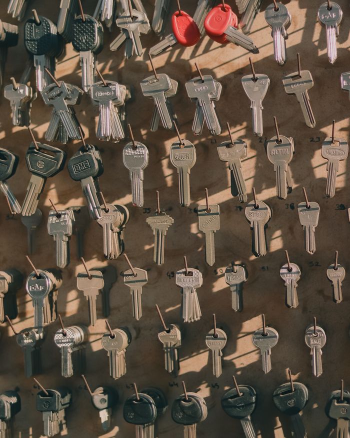 services-02 A collection of assorted metal keys hanging on a wall with hooks, casting shadows.