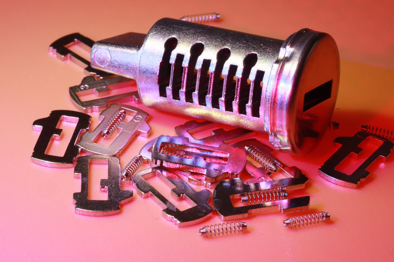 services-01 Detailed image of a disassembled lock cylinder and its metal components on a colored surface.