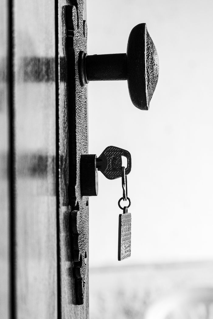 services-04 Close-up of a key in an antique lock on a rustic door, black and white.