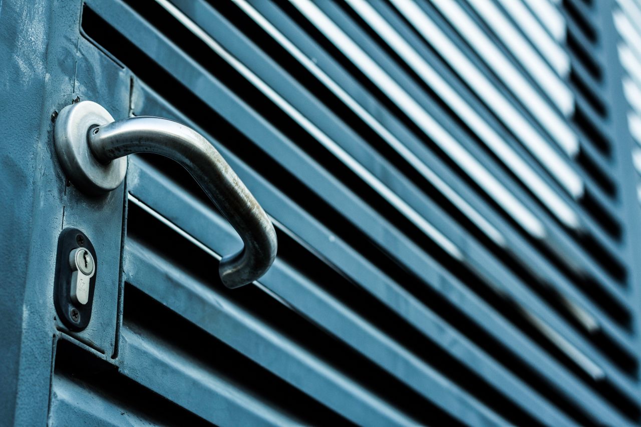 about-img Close-up of a sleek stainless steel door handle and lock on a blue metallic door.