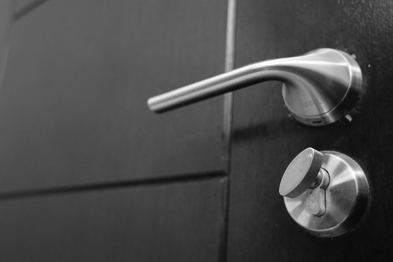 ours-journey Black and white photo capturing a sleek stainless steel door handle with a focus on style and security.